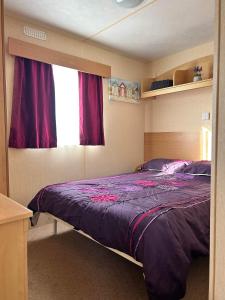 a bedroom with a bed with purple sheets and a window at Lyntons 3 bedroom caravan pets stay free in Heacham