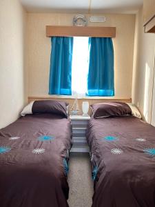two beds in a room with blue curtains and a window at Lyntons 3 bedroom caravan pets stay free in Heacham