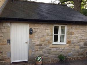 a stone cottage with a white door and two windows at Lesbury Lodge - (a 'bijou residence') with hot tub in Alnwick