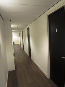 un pasillo vacío con puerta negra y suelo de madera en 3BE Backpackers Bed & Breakfast Eindhoven en Eindhoven