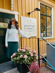una mujer de pie junto a un cartel en un edificio en Klostergårdens Vandrarhem, en Varnhem