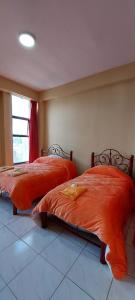 two beds with orange sheets in a room with a window at Hostal El Paraiso in Tarija