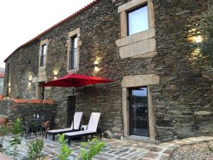 a stone building with two chairs and an umbrella at Castas do Douro in Tabuaço