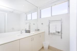 a white bathroom with a sink and a window at Cottesloe Azura Apartment in Perth