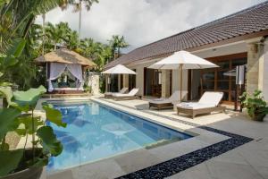 a pool with chairs and umbrellas next to a house at Villa Alu Lima in Seminyak