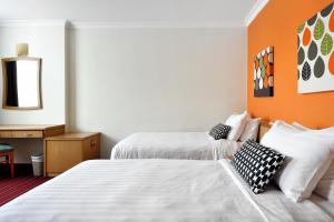 two beds in a hotel room with an orange wall at The Assembly Place at Stevens, Service Residences in Singapore