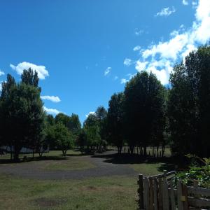 a park with trees and a fence and a blue sky at Cabaña las gotas coñaripe in Coñaripe +3 photos
