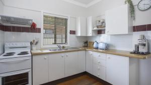 a white kitchen with white cabinets and a sink at Coast Along - Ettalong Beach in Ettalong Beach
