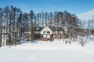 a house in the snow in front of trees at Adagio Hokkaido in Biei