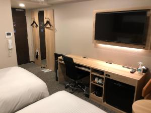 a hotel room with a desk with a television on a wall at Smile Hotel Osaka Nakanoshima in Osaka
