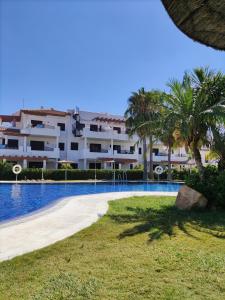 duży apartamentowiec z basenem i palmami w obiekcie APARTAMENTO EN COTO DE SANCTI PETRI w mieście Chiclana de la Frontera