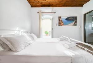 a white bedroom with two beds and a view of the ocean at Serenity View - traditional village apartment in Kousés