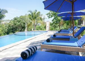 a row of blue lounge chairs with umbrellas next to a pool at Penida Sunset Ocean View Bungalows in Nusa Penida