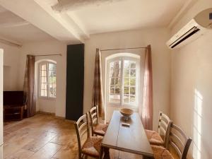 a dining room with a table and chairs and two windows at Domaine Bellefontaine in Aix-en-Provence