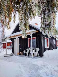 a black cabin with a table and chairs in the snow at Self Check-in Sauna Cabin next to Hiking Trails in Kärde