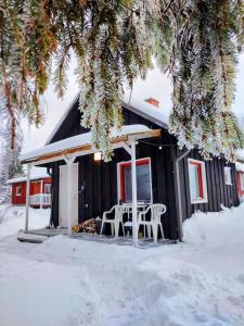 a black cabin with a table and chairs in the snow at Self Check-in Sauna Cabin next to Hiking Trails in Kärde