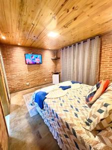 1 dormitorio con 1 cama y TV en una pared de ladrillo en Pousada Recanto Ninho Verde Chalés, en Campos do Jordão