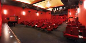 an empty auditorium with red chairs and a grand piano at PASTORI - Das historische Lichtspielgasthaus in Weilmünster
