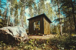 Venejoen Piilo - Naava في Romppala: كابينة خشبية صغيرة في غابة بها صخرة كبيرة