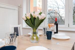 a vase of pink flowers on a table with a bottle of wine at Cozy studio in Downtown Gdańsk by Renters in Gdańsk