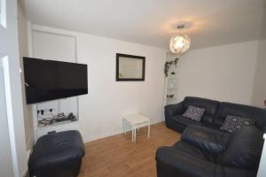 a living room with a black leather couch and a flat screen tv at Mountain Escape - Cosy 2 bed house in Afan Valley in Port Talbot