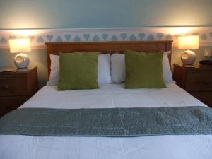 a bedroom with a bed with green pillows and two lamps at The Denewood in Sandown