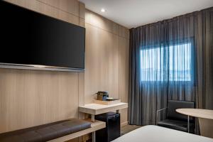 um quarto de hotel com uma televisão de ecrã plano e uma cadeira em AC Hotel Sants by Marriott em Barcelona
