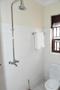 a white bathroom with a shower and a toilet at Golden Cherries Guest House in Jinja