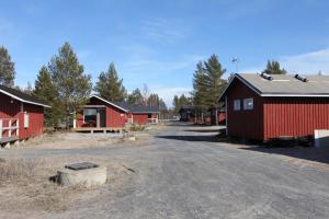a group of red barns with a dirt road in front at Rantasumppu 14, mökki viilennyksellä in Hailuoto
