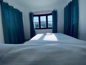 een slaapkamer met een bed met blauwe gordijnen en een raam bij Tranquiland in Kodaikānāl