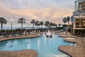 a resort pool with tables and chairs and palm trees at Courtyard by Marriott Myrtle Beach Oceanfront in Myrtle Beach