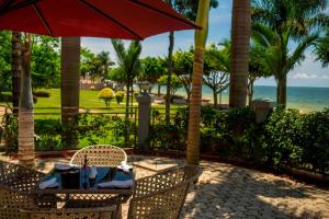 Protea Hotel by Marriott Entebbe في عنتيبي: طاولة وكراسي مع مظلة حمراء والمحيط