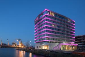un edificio alto con luces moradas en él junto a un río en Moxy Amsterdam Houthavens, en Ámsterdam