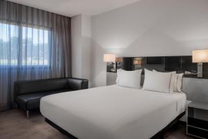 um quarto de hotel com uma grande cama branca e uma cadeira em AC Hotel Murcia by Marriott em Múrcia