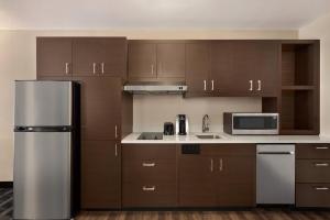 La cuisine est équipée de placards bruns et d'un réfrigérateur en acier inoxydable. dans l'établissement TownePlace Suites Cedar Rapids Marion, à Marion
