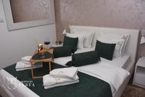 a white bed with green and white pillows and a table at VESTA Apartman in Sremska Mitrovica