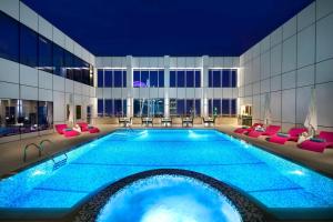 een groot zwembad in een hotel met rode stoelen en een groot gebouw bij Courtyard by Marriott Riyadh Olaya in Riyad
