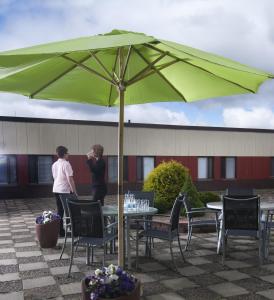 due donne in piedi sotto un ombrellone verde su un patio di Best Western Nya Star Hotel ad Avesta