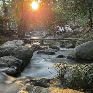 a river with rocks and the sun in the background at เดอะริเวอร์ แม่กำปอง The River Maekampong Chiang Mai in Ban Pok Nai