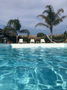 una piscina di acqua blu con due sedie e palme di Verter Home Resort a Ovile la Marina