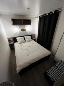 Habitación pequeña con cama y cortina negra en MOBIL-HOME CONFORTABLE ET BIEN EQUIPE AVEC PISCINES ET LA PLAGE A PIED, en Fouesnant