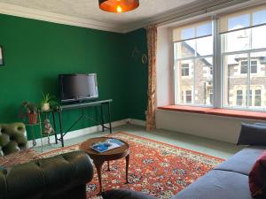 a green living room with a couch and a tv at Squirrel Away At Leven House in Crieff