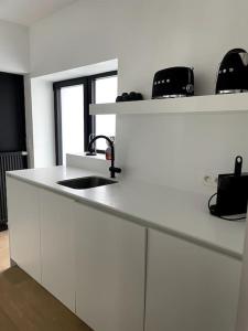 een witte keuken met een wastafel en twee zwarte stoelen bij Cofa'sea designvol appartement in Knokke-Heist