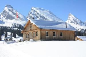 een houten huis in de sneeuw met bergen op de achtergrond bij Casa Uccello in Wildhaus