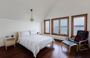 a bedroom with a bed and a chair and windows at WhidbeyBeachHouse, an Oceanfront Getaway on a Private Beach in Langley