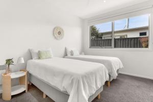 2 camas en una habitación blanca con ventana en Pukeko Beach House en Rhyll