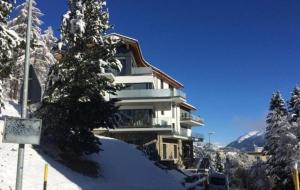 dom pokryty śniegiem z drzewem przed nim w obiekcie Chavallera Casa Torri w Sankt Moritz