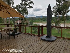 eine Holzterrasse mit einem Tisch und einem Surfbrett in der Unterkunft Resort D Rumah Bonda River View Kuala Kangsar in Kampong Senawar