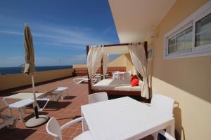 balcón con sillas y mesas blancas y sombrilla en Apartamentos Isla Tenerife Sur en Los Abrigos