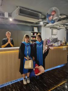 Duas mulheres em vestes de formatura, ao balcão. em The Key Point Hotel em Bangkok